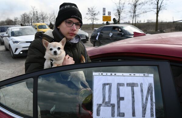 Молодой человек с собакой на руках возле машины на выезде из Мариуполя - Sputnik Азербайджан