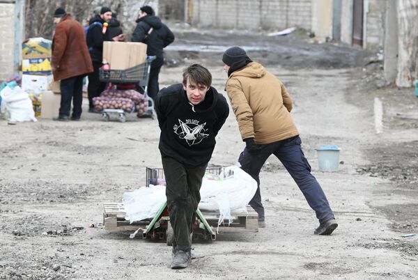 Молодой человек тянет тележку с продуктами в Мариуполе - Sputnik Азербайджан