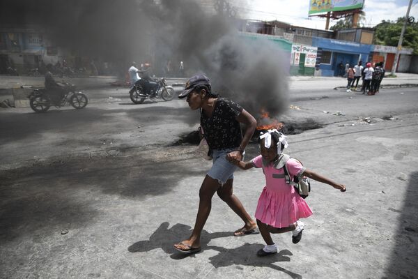 Женщина ведет ребенка мимо демонстрации против роста насилия в Порт-о-Пренс, Гаити. - Sputnik Азербайджан