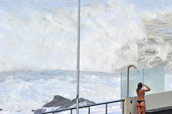 Девушка принимает душ после купания на фоне гигантских волн на пляже Бонди в Сиднее. - Sputnik Азербайджан