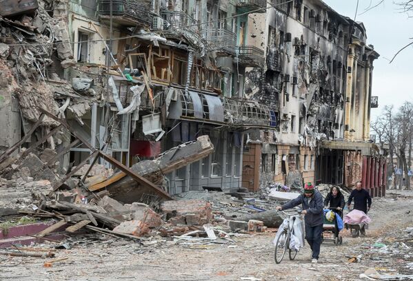 Жители Мариуполя идут по улице города мимо разрушенных домов - Sputnik Азербайджан