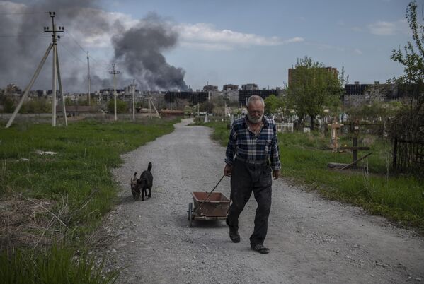 Мужчина везет тележку с травой неподалеку от металлургического комбината Азовсталь в Мариуполе - Sputnik Азербайджан