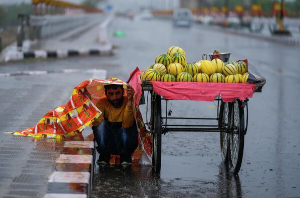 Продавец фруктов укрывается во время дождя в индийском городе Джамму. - Sputnik Азербайджан