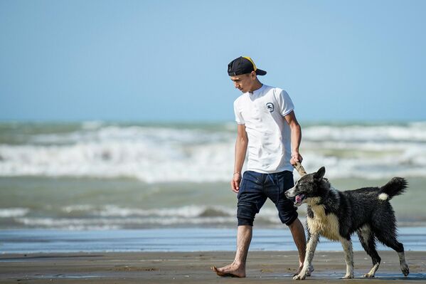 Молодой человек вместе со своей собакой гуляет на берегу моря в Баку. - Sputnik Азербайджан
