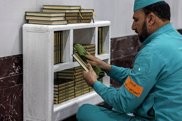 Работник Большой мечети протирает книги Священного Корана, чтобы подготовить их для верующих во время ежегодного хаджа. - Sputnik Азербайджан