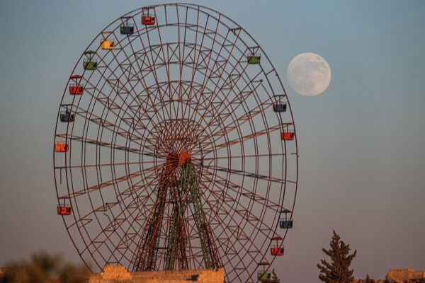 Полная луна и колесо обозрения в заброшенном детском парке развлечений недалеко от Аль-Найраб, провинция Идлиб, Сирия. - Sputnik Азербайджан
