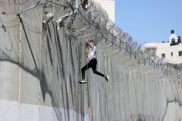 Юноша спускается по веревке через бетонную стену израильского разделительного барьера в район Бейт-Ханина в Восточном Иерусалиме. - Sputnik Азербайджан