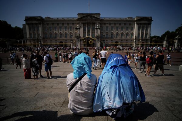 Люди сидят, закрыв головы от солнца у Букингемского дворца в Лондоне. - Sputnik Азербайджан