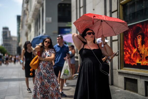 Женщина держит зонтик, чтобы укрыться от солнца в жаркий солнечный день в Мадриде, Испания. - Sputnik Азербайджан