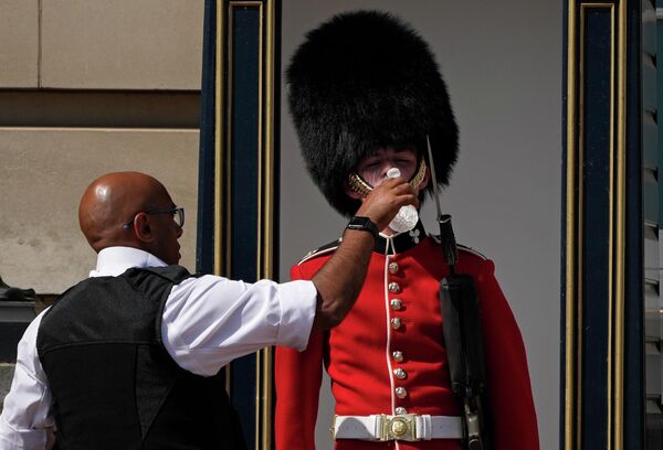 Полицейский поит британского солдата в традиционной медвежьей шапке, дежурящего у Букингемского дворца, в жаркую погоду в Лондоне. - Sputnik Азербайджан