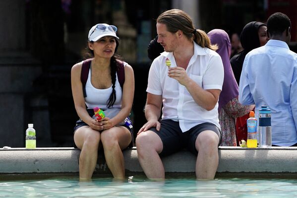 Пара ест мороженое, опуская ноги в фонтан на Трафальгарской площади в центре Лондона. - Sputnik Азербайджан