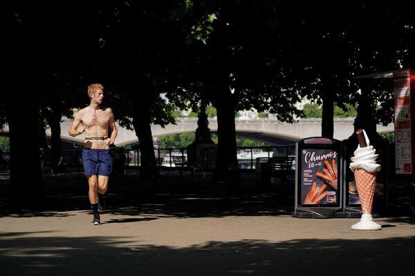 Мужчина пробегает мимо вывески с мороженым на южном берегу Темзы в Лондоне. - Sputnik Азербайджан