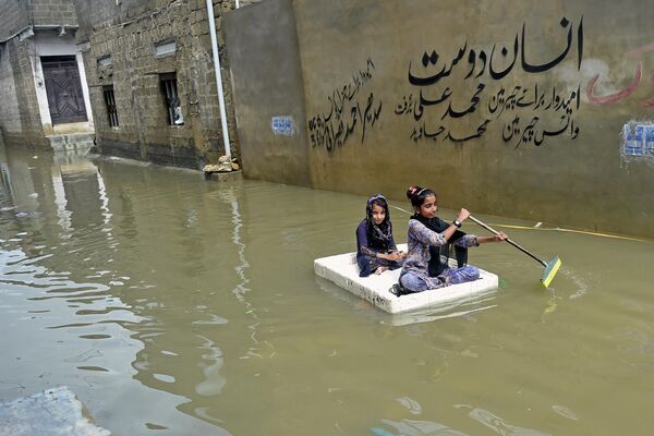 Девочки перебираются на плоту через затопленную после сильных дождей улицу в жилом районе Карачи, Пакистан. - Sputnik Азербайджан