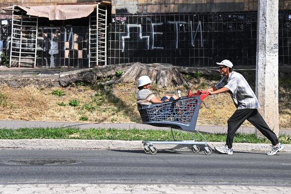 Мужчина везет женщину в торговой тележке по улице в Мариуполе - Sputnik Азербайджан