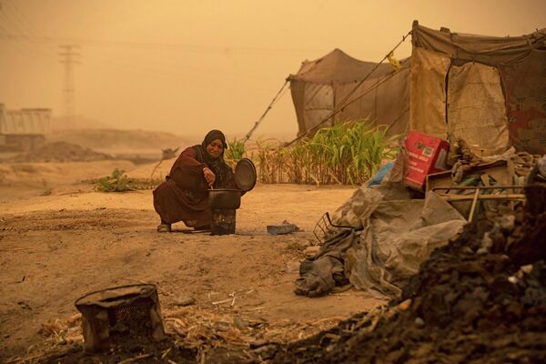 Женщина готовит во время песчаной бури в лагере для беженцев в пригороде Ракки на севере Сирии. - Sputnik Азербайджан