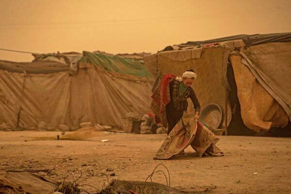 Молодой человек несет вещи во время песчаной бури в лагере для беженцев в пригороде Ракки на севере Сирии. - Sputnik Азербайджан