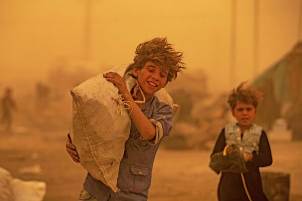 Юноша идет во время песчаной бури в лагере для беженцев в пригороде Ракки на севере Сирии. - Sputnik Азербайджан