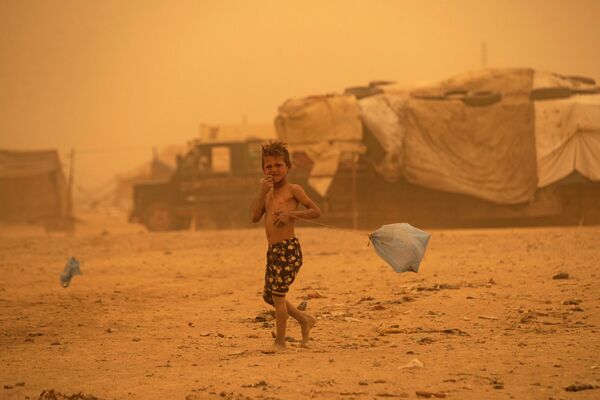 Мальчик идет во время песчаной бури в лагере для беженцев в пригороде Ракки на севере Сирии. - Sputnik Азербайджан