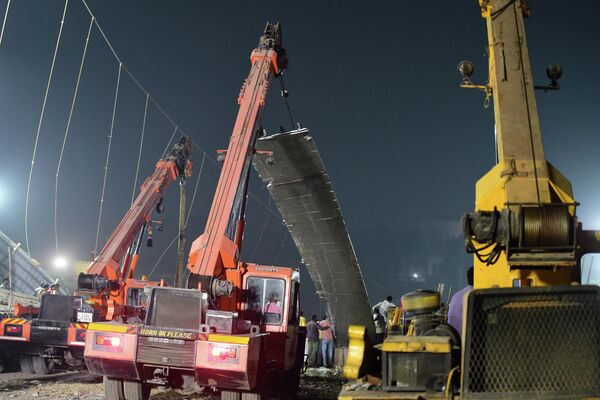 Рабочие снимают секцию обрушившегося подвесного моста через реку Маччху в городе Морви, Индия. - Sputnik Азербайджан