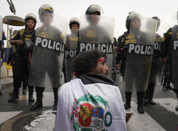 Мужчина сидит напротив шеренги полицейских во время марша против президента Перу Дины Болуарте в Лиме, Перу. - Sputnik Азербайджан