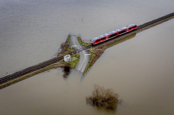 Поезд приближается к железнодорожному переезду между затопленными полями в Ниддерау-Айхен недалеко от Франкфурта, Германия. - Sputnik Азербайджан