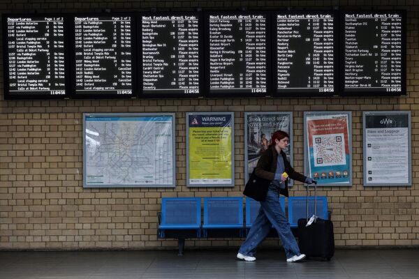Пассажир с чемоданом проходит мимо табло отправления, показывающего отмененные поезда во время национальной забастовки, на вокзале Рединг. - Sputnik Азербайджан