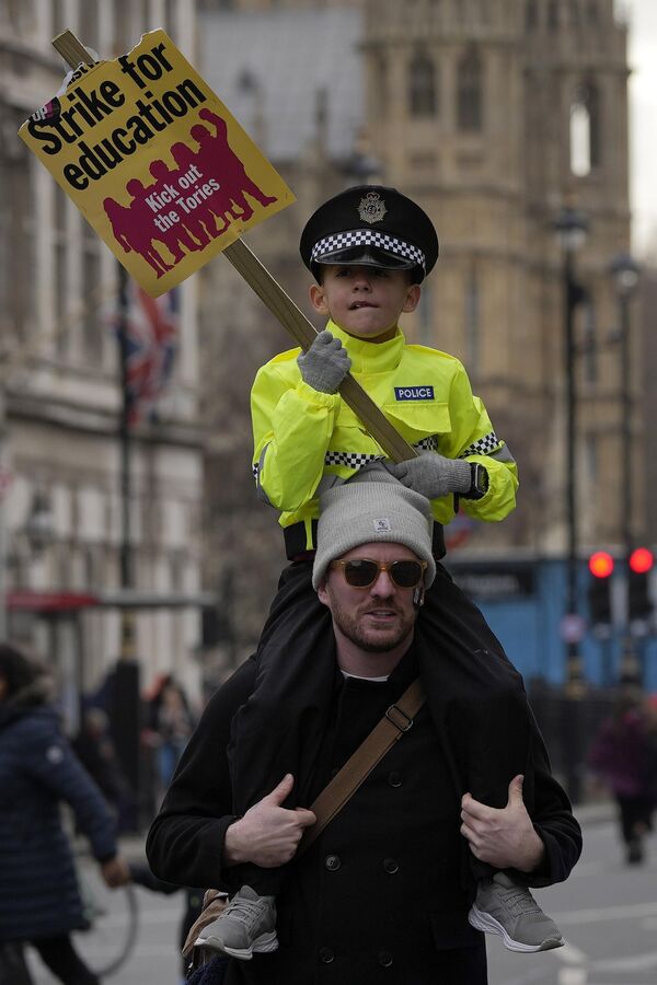 Мужчина с маленьким мальчиком на плечах, одетый как полицейский, показывает плакат во время марша протеста в Лондоне. - Sputnik Азербайджан