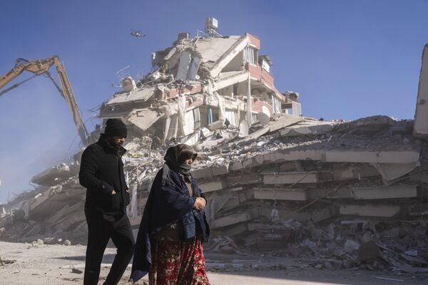 Местные жители прогуливаются перед разрушенным зданием в Нурдаги, на юге Турции. - Sputnik Азербайджан