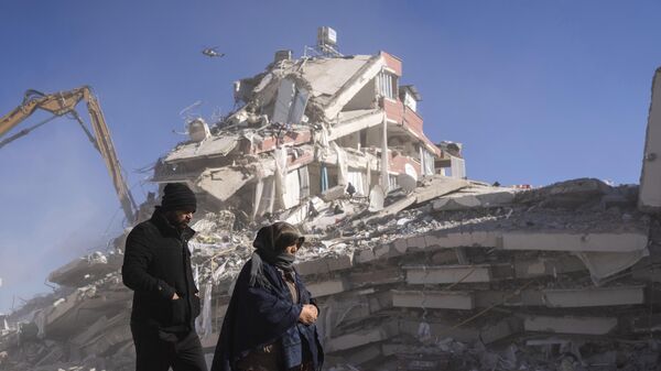 Местные жители прогуливаются перед разрушенным зданием в Нурдаги, на юге Турции - Sputnik Азербайджан
