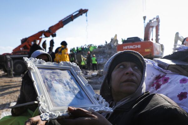 Мужчина с фоторамкой на фоне спасателей, которые ищут выживших среди разрушенных зданий в Нурдаги на юге Турции. - Sputnik Азербайджан