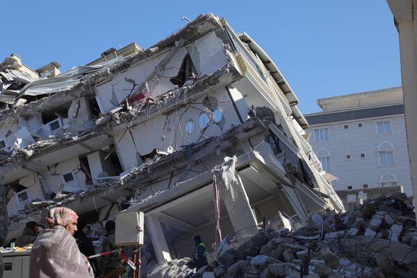 Женщина стоит перед рухнувшим зданием в Ислахии, в сильно пострадавшем регионе Газиантеп в пограничном районе Турции и Сирии. - Sputnik Азербайджан