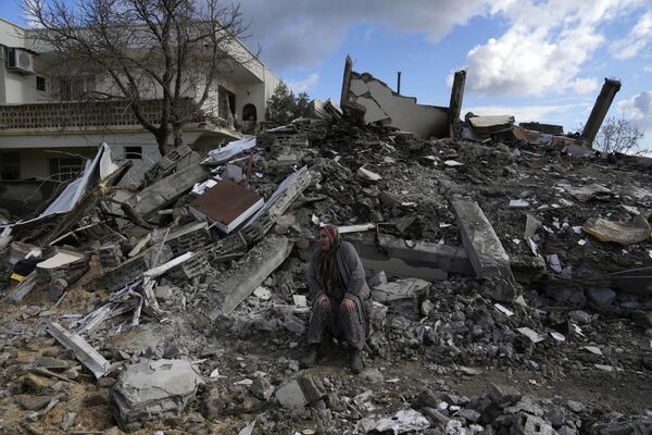 Женщина сидит на развалинах, пока спасатели ищут людей под остатками разрушенных зданий в городе Нурдаги, Турция. - Sputnik Азербайджан