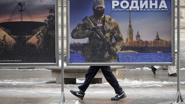 Мужчина проходит мимо стенда с изображением российского военнослужащего и надписью «Родина, которую мы защищаем»  - Sputnik Азербайджан