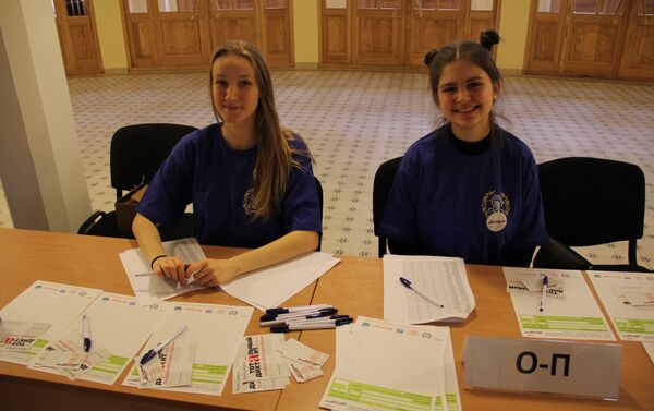 Девушки-студентки за столами выдавали зарегистрировавшимся участникам диктанта листы, ручки и карточки участников - Sputnik Азербайджан