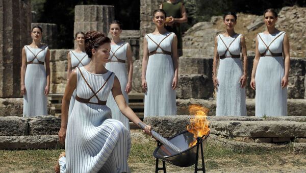 Греческая актриса Катерина Леху, играющая роль верховной жрицы, зажигает факел от солнечных лучей, отраженных в параболическом зеркале - Sputnik Азербайджан