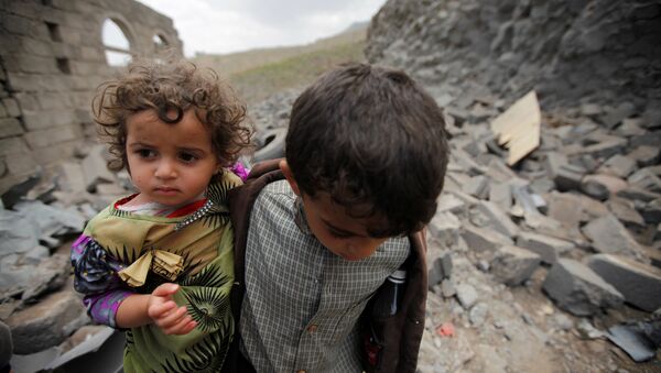 Мальчик несет свою сестру, по обломками дома который был разрушен авиаударом коалиции во главе с Саудовской Аравией - Sputnik Азербайджан