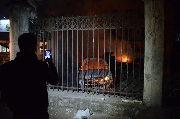 Человек фотографирует на смартфон сожженные в ходе беспорядков в Батуми машины - Sputnik Азербайджан