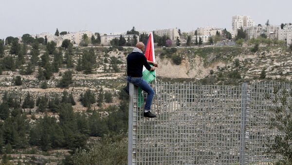 Мужчина прикрепляет национальный флаг Палестины на железный забор, установленный израильскими силами безопасности между палестинской деревней Бейт-Джала и Иерусалимом, 30 марта 2017 года  - Sputnik Azərbaycan
