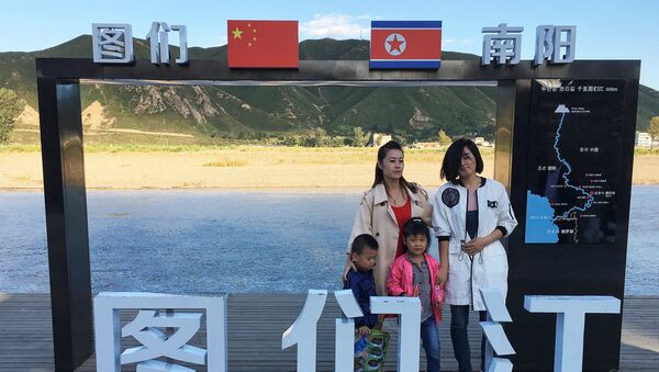 Туристы фотографируются на фоне постера на границе между Северной Кореей и Китаем, 30 августа 2017 года - Sputnik Азербайджан