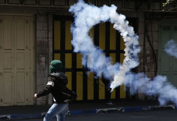 Палестинский демонстрант бросает газовую шашку в израильских солдат во время столкновений на Западном берегу реки Иордан - Sputnik Азербайджан