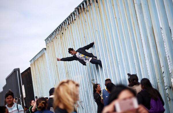 Участник демонстрации мигрантов из Центральной Америки на заборе, разделяющем Мексику и США на границе в Тихуане, Мексика - Sputnik Азербайджан