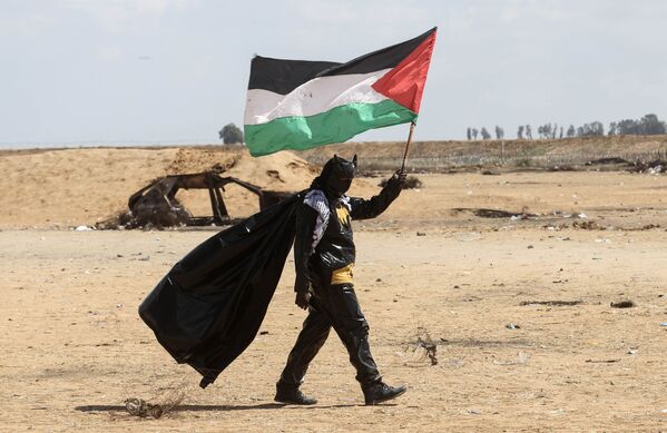 Палестинский демонстрант в костюме Бэтмена с национальным флагом возле границы между Израилем и Газой - Sputnik Азербайджан