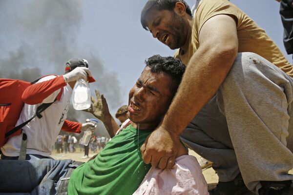 Палестинец помогает раненому демонстранту во время столкновений с израильскими военными в районе границы между Израилем и сектором Газа - Sputnik Азербайджан