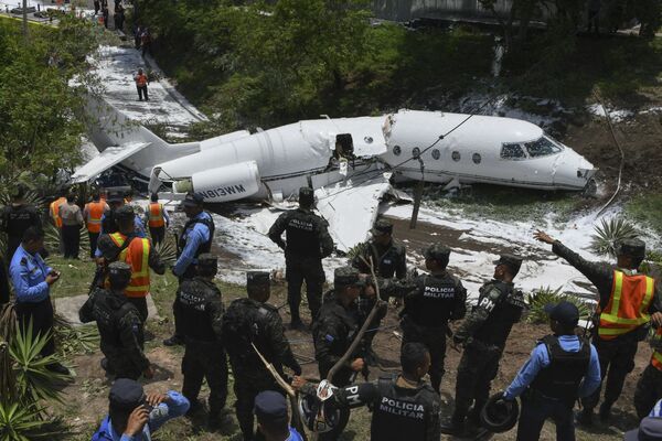 Полиция и спасатели работают у самолета, выкатившийся за пределы взлетно-посадочной полосы и развалившегося на части после приземления в международном аэропорту Тонконтин в Тегусигальпе, Гондурас - Sputnik Азербайджан