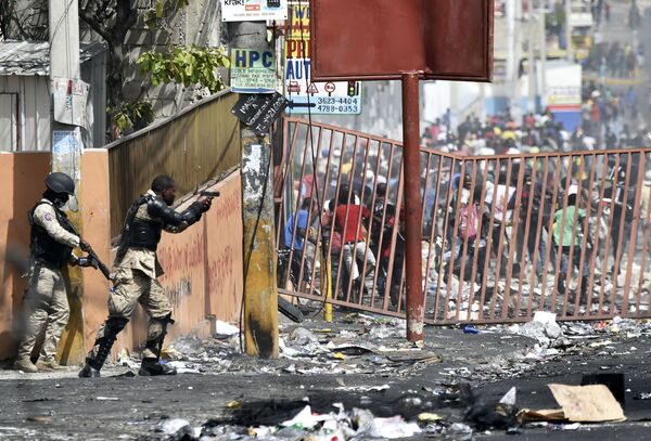 Полицейский направляет пистолет на людей, чтобы избежать мародерства во время протестов против повышения цен на топливо близ столицы Гаити - Sputnik Азербайджан