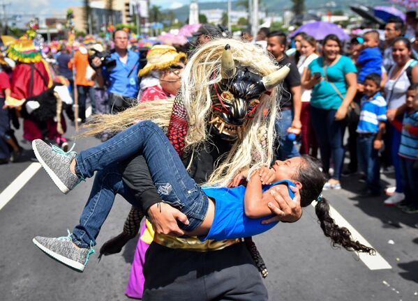 Человек в маске мифологического существа держит на руках девочку во время парада в Сан-Сальвадор - Sputnik Азербайджан