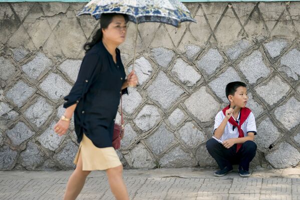Девушка с зонтиком проходит мимо сидящего мальчика в Пхеньяне - Sputnik Азербайджан