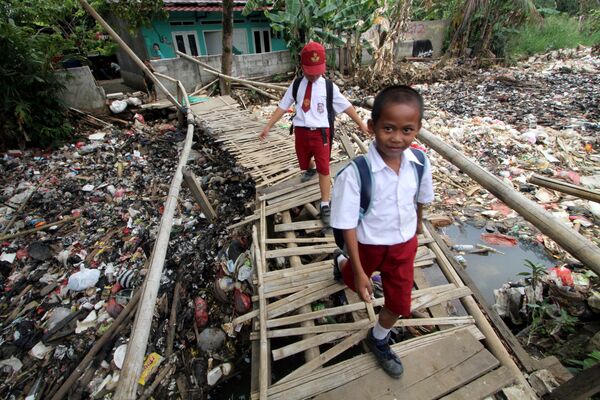 Школьники идут по бамбуковому мосту над заполненным мусором рукаве реки Чиливунг в Индонезии - Sputnik Азербайджан