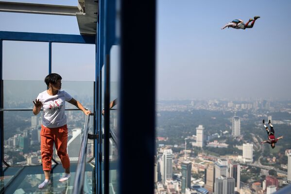 Турист наблюдает, как бейсджамперы прягают со смотровой площадки телебашни Менара Куала-Лумпур, Малайзия - Sputnik Азербайджан