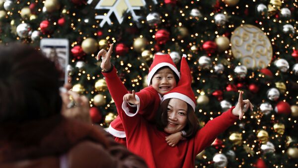 Женщина и ее ребенок в шапках Санта-Клауса позируют для сувенирной фотографии в торговом центре в Пекине, воскресенье, декабрь 25, 2016 - Sputnik Azərbaycan